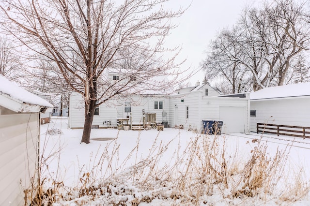 snow covered rear of property with an attached garage and fence