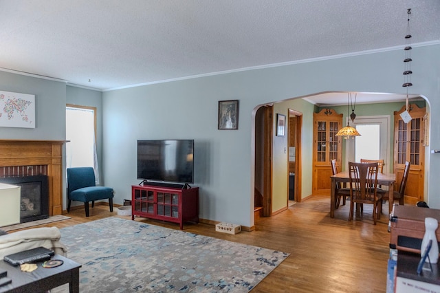 living room with arched walkways, a textured ceiling, a fireplace with flush hearth, wood finished floors, and ornamental molding