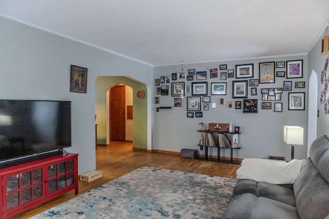 living area featuring ornamental molding, arched walkways, baseboards, and wood finished floors