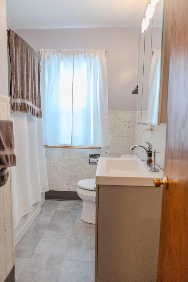 full bathroom with toilet, a wainscoted wall, vanity, tile walls, and tile patterned floors