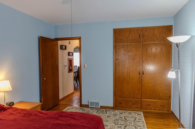 bedroom with baseboards, visible vents, a ceiling fan, wood finished floors, and a closet