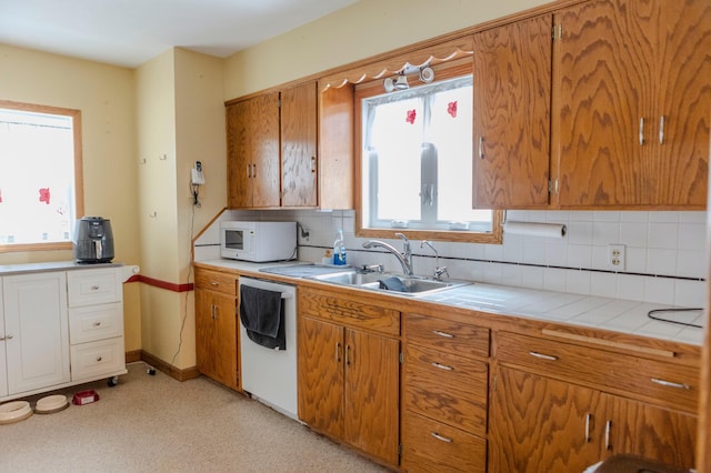 kitchen with brown cabinets, tile counters, backsplash, a sink, and white appliances