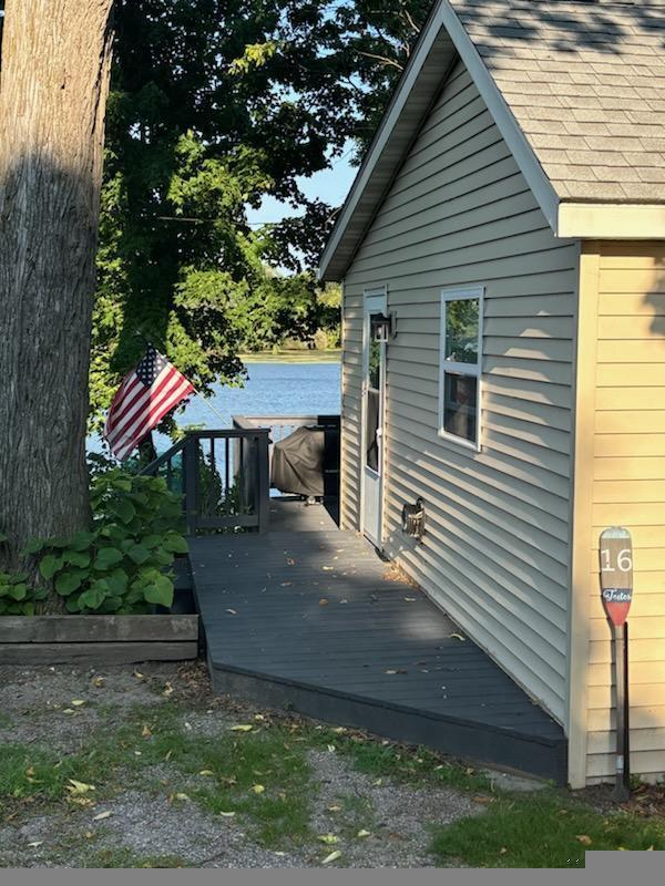 view of side of property featuring a deck with water view and roof with shingles