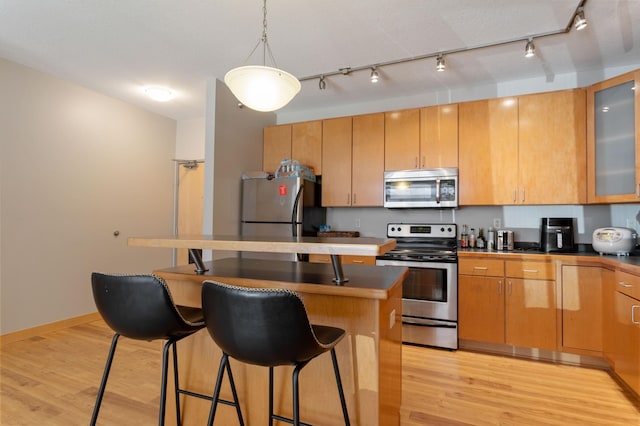 kitchen with a kitchen island, a kitchen breakfast bar, appliances with stainless steel finishes, light wood-type flooring, and glass insert cabinets