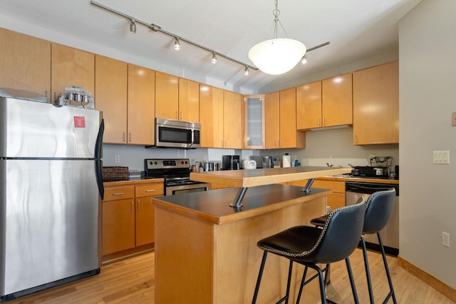 kitchen featuring light wood-style flooring, appliances with stainless steel finishes, a center island, a kitchen bar, and glass insert cabinets