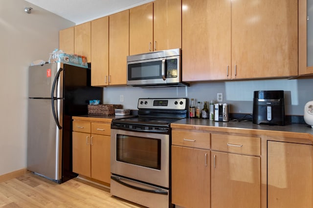 kitchen featuring stainless steel appliances, dark countertops, light wood-style flooring, and baseboards