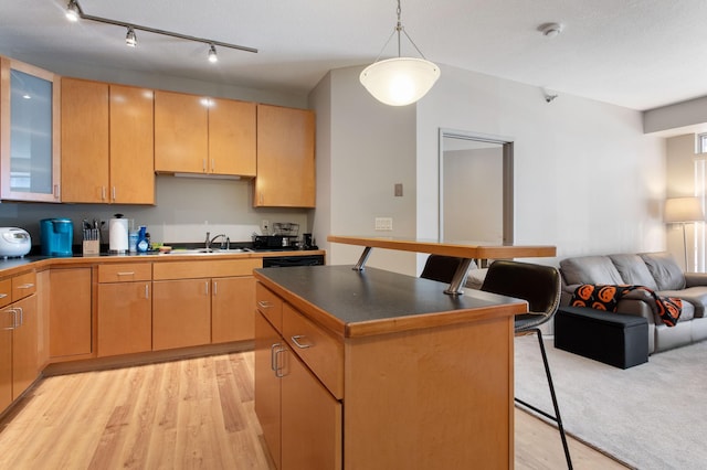 kitchen with a breakfast bar, light wood finished floors, dark countertops, open floor plan, and a sink