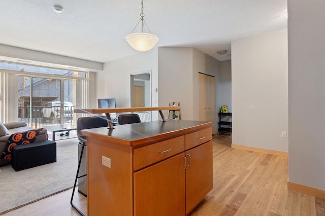 kitchen featuring light wood finished floors, baseboards, open floor plan, a breakfast bar, and pendant lighting