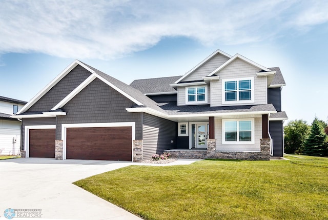 craftsman house with roof with shingles, a front yard, a garage, stone siding, and driveway