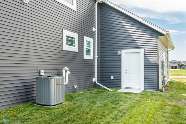 rear view of property with central AC unit and a lawn