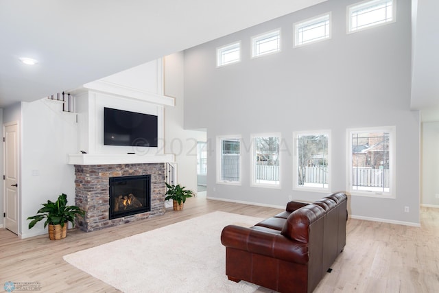 living area featuring a glass covered fireplace, wood finished floors, baseboards, and a towering ceiling