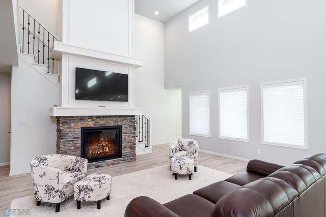 living room with stairway, baseboards, a stone fireplace, and light wood finished floors