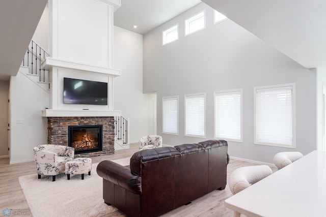 living area featuring a stone fireplace, baseboards, light wood-type flooring, and a towering ceiling