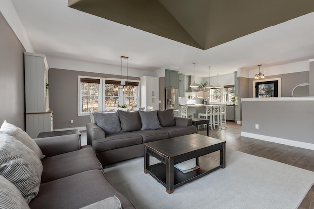 living area featuring dark wood-style floors, a notable chandelier, high vaulted ceiling, and baseboards