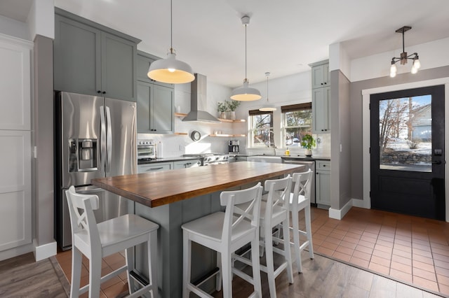 kitchen with butcher block counters, a kitchen breakfast bar, appliances with stainless steel finishes, backsplash, and wall chimney exhaust hood