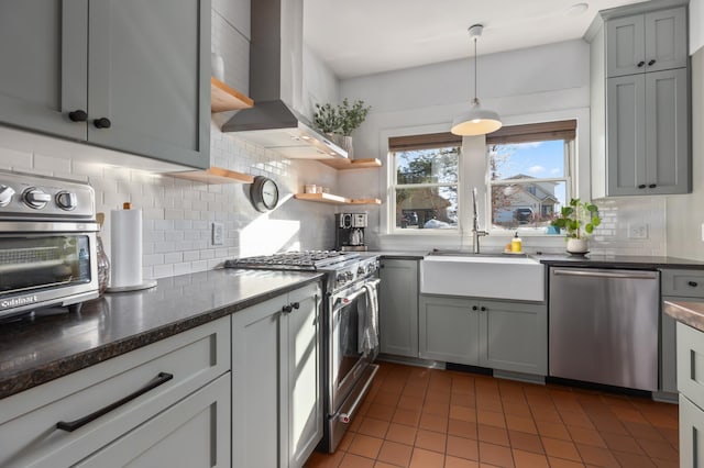 kitchen with a sink, appliances with stainless steel finishes, wall chimney range hood, gray cabinets, and backsplash