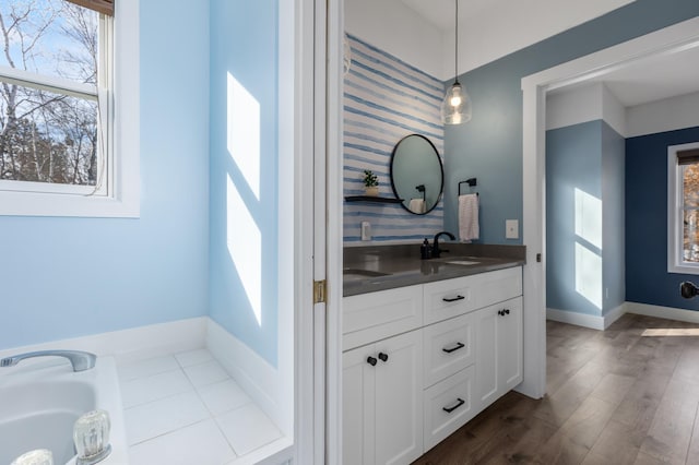 bathroom featuring a bathtub, double vanity, a sink, wood finished floors, and baseboards