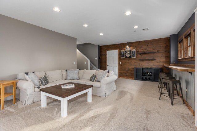 living area with recessed lighting, wooden walls, stairs, and light colored carpet