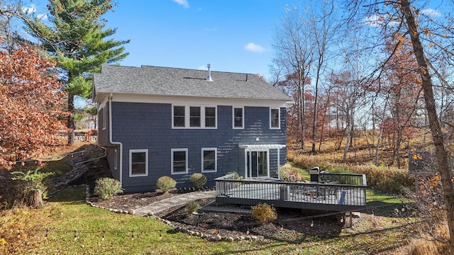 rear view of property with roof with shingles, a wooden deck, and a lawn