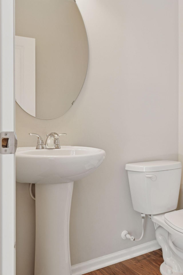 half bathroom featuring a sink, baseboards, toilet, and wood finished floors