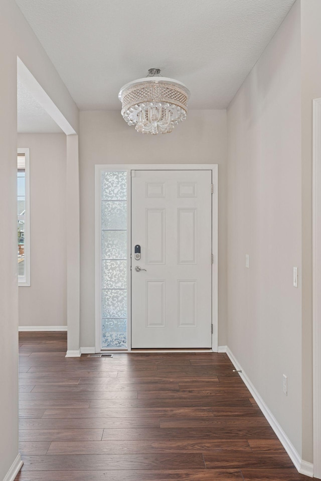 foyer entrance featuring dark wood-style floors, a notable chandelier, baseboards, and a wealth of natural light