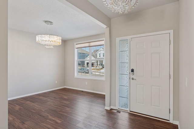 foyer featuring dark wood finished floors, a textured ceiling, baseboards, and an inviting chandelier