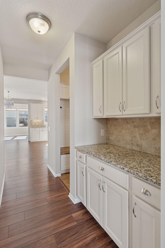 kitchen with backsplash, white cabinetry, dark wood-type flooring, and light stone countertops