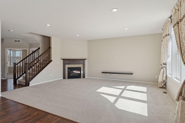 unfurnished living room featuring visible vents, wood finished floors, a glass covered fireplace, recessed lighting, and stairs