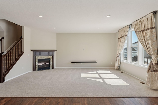 unfurnished living room with stairway, wood finished floors, baseboards, recessed lighting, and a glass covered fireplace