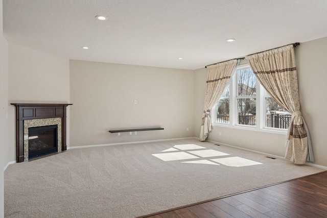 unfurnished living room with wood finished floors, visible vents, baseboards, a premium fireplace, and recessed lighting