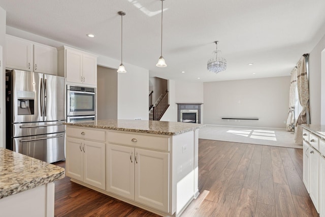 kitchen featuring light stone countertops, pendant lighting, appliances with stainless steel finishes, a fireplace, and wood finished floors