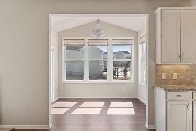 unfurnished dining area featuring baseboards, lofted ceiling, and wood finished floors