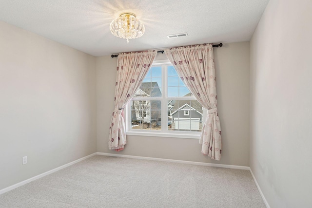 empty room featuring baseboards, visible vents, a textured ceiling, carpet flooring, and a notable chandelier