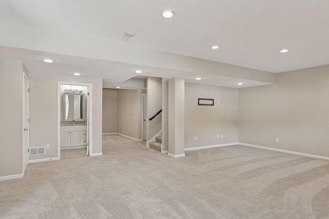 finished below grade area featuring visible vents, baseboards, light colored carpet, and stairway