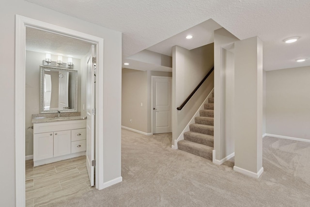 corridor featuring baseboards, recessed lighting, a sink, a textured ceiling, and light colored carpet