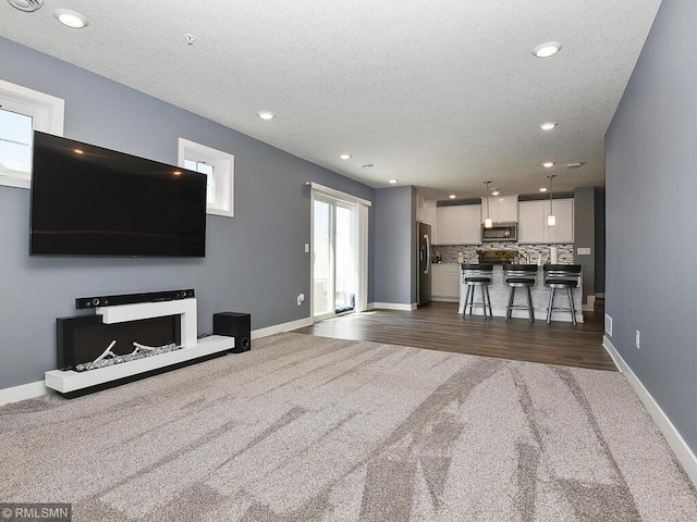 unfurnished living room featuring dark carpet, a textured ceiling, and baseboards