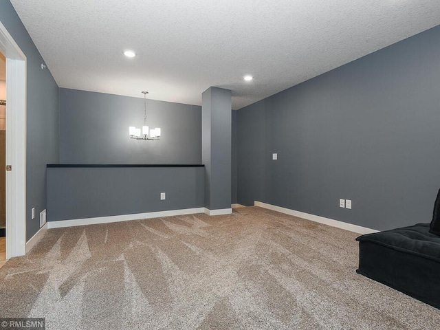 carpeted spare room featuring a textured ceiling, baseboards, and a notable chandelier