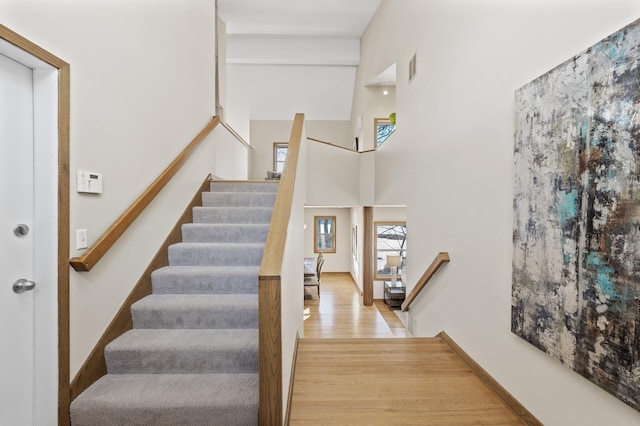 stairs with a towering ceiling, baseboards, visible vents, and wood finished floors