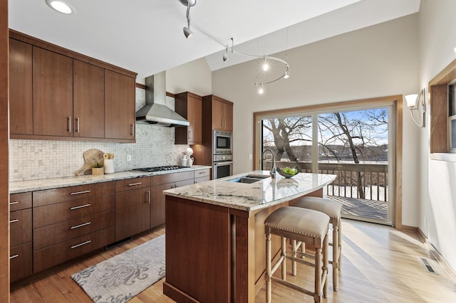 kitchen with stainless steel gas cooktop, visible vents, a sink, wall chimney range hood, and a kitchen bar