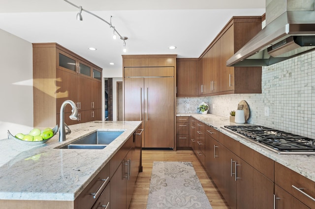 kitchen featuring light wood finished floors, stainless steel gas stovetop, a sink, wall chimney range hood, and paneled refrigerator