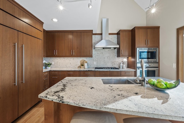 kitchen with built in appliances, light stone counters, a kitchen breakfast bar, wall chimney range hood, and backsplash