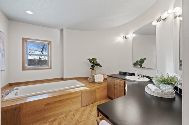 full bath featuring a garden tub, a textured ceiling, and vanity