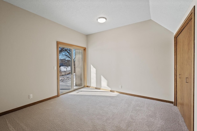 spare room featuring carpet floors, baseboards, a textured ceiling, and lofted ceiling