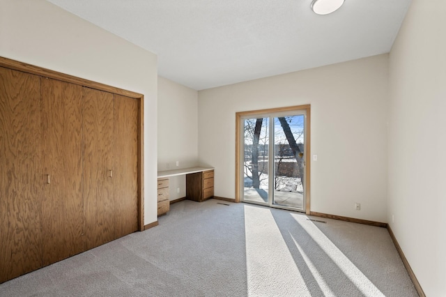 unfurnished bedroom featuring access to outside, baseboards, light colored carpet, and built in study area