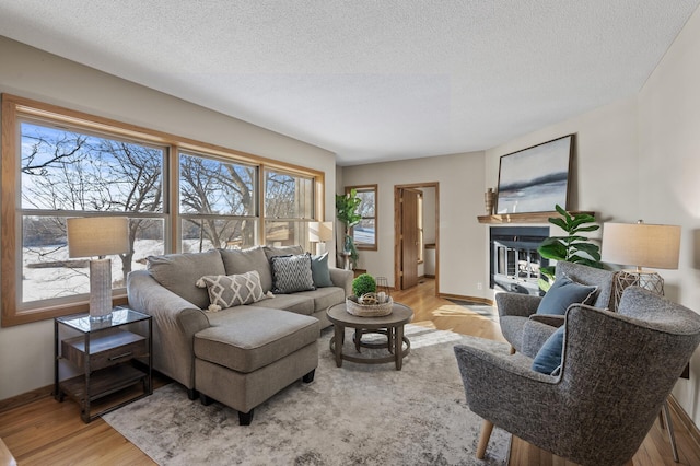 living area with light wood-style floors, a glass covered fireplace, a textured ceiling, and baseboards