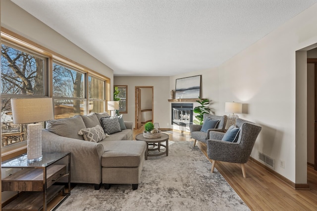 living room with a textured ceiling, wood finished floors, visible vents, and baseboards