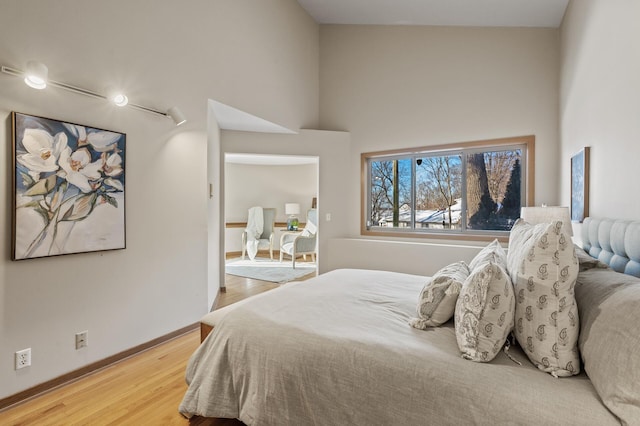 bedroom with baseboards, a towering ceiling, and light wood-style floors