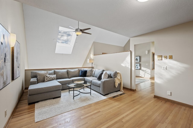 living room with vaulted ceiling with skylight, light wood-style flooring, visible vents, and ceiling fan