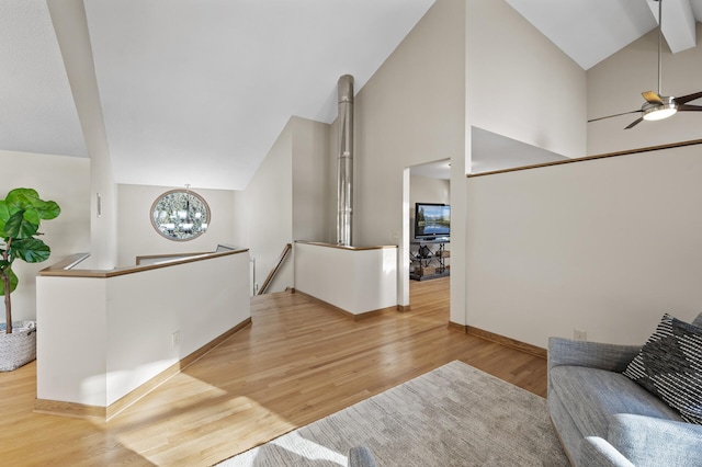 living area with high vaulted ceiling, ceiling fan with notable chandelier, baseboards, and wood finished floors