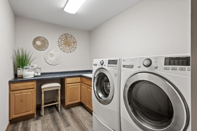 clothes washing area with a textured ceiling, washer and clothes dryer, wood finished floors, and cabinet space